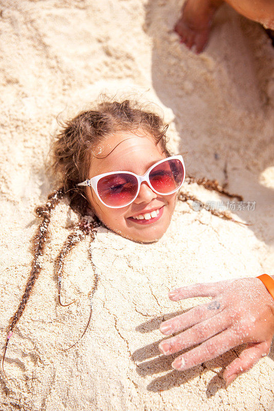 年轻无忧无虑的女孩被埋在沙滩上的沙子下