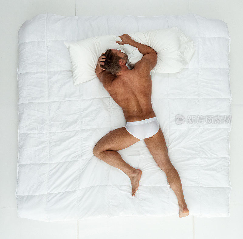 男性躺在卧室的白色背景前，穿着赛车内裤