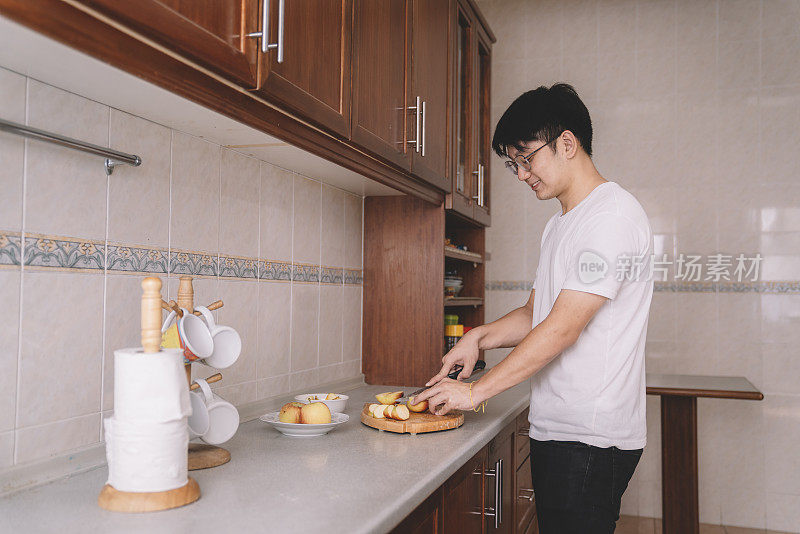 早上，一位亚洲华人男子在厨房里准备早餐和切苹果