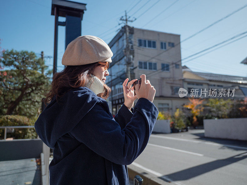 美丽的年轻女孩在城市里用智能手机拍照。