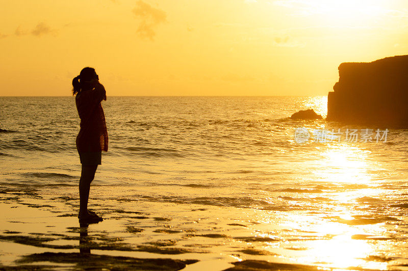 亚洲女人站在海边的海滩在日落