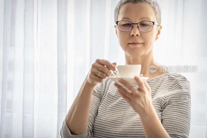 一个站在窗边喝着咖啡的成熟女人