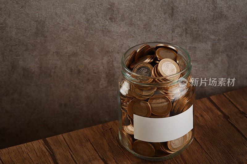 硬币储蓄罐与空白标签装满现金的桌子和水泥墙为背景