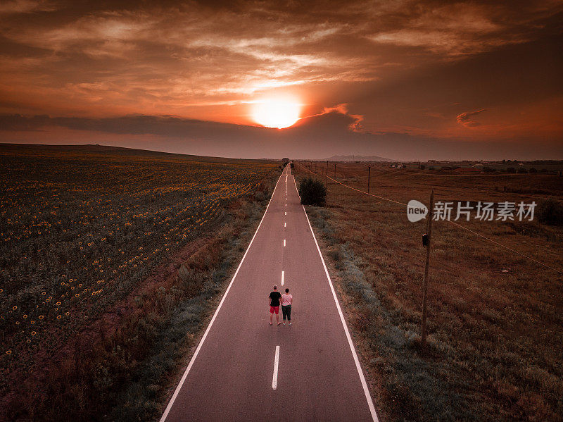 高角度的夫妻一起走在笔直的乡村道路进入日落
