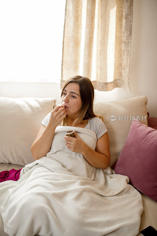 患流感的妇女在客厅的沙发上盖着毯子吃药
