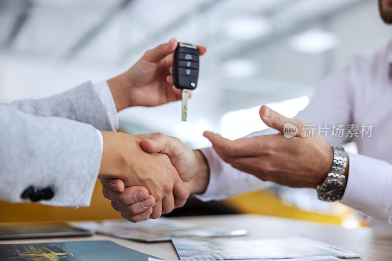 汽车卖家和买家握手的特写。汽车卖家把车钥匙交给买家。汽车沙龙内部。