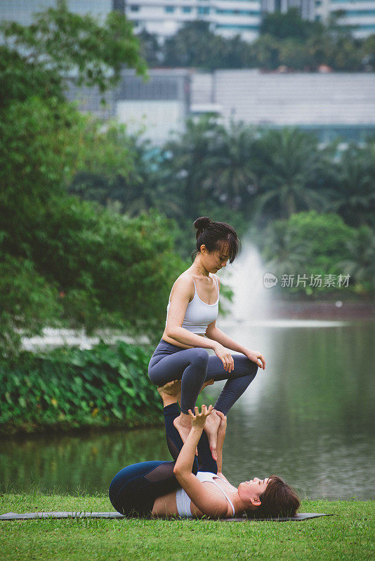 两个年轻的健身亚洲妇女一起练习Acroyoga放松在城市公园