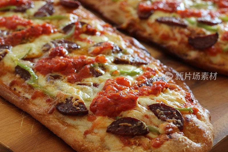 特写自制披萨切片在木砧板上，披萨与青椒，香肠，番茄酱和奶酪
