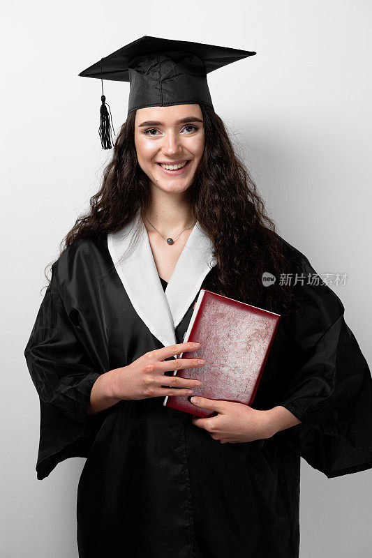 学生在毕业长袍和帽子书准备完成大学。未来的科学领袖。身着黑色长袍的年轻女院士微笑着。