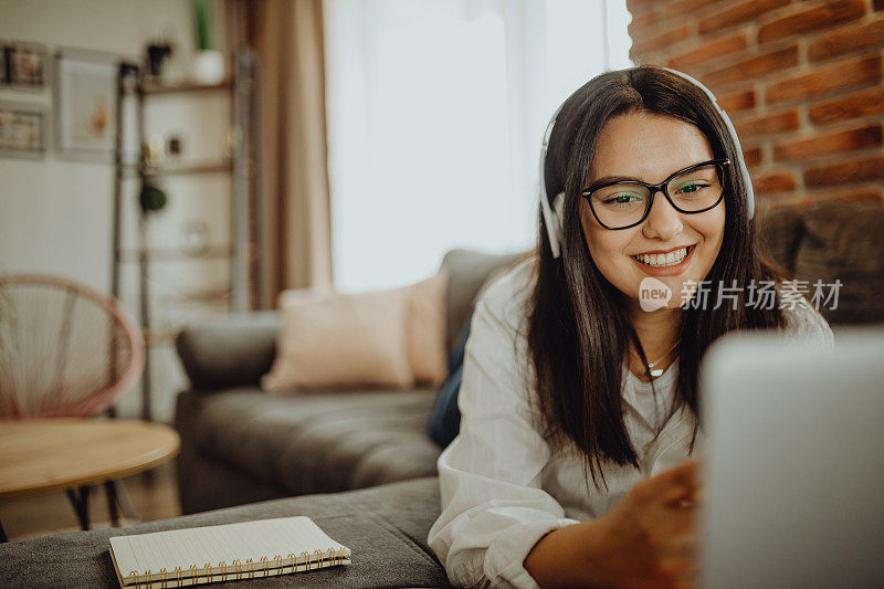 一位年轻的女学生坐在沙发上使用笔记本电脑耳机学习