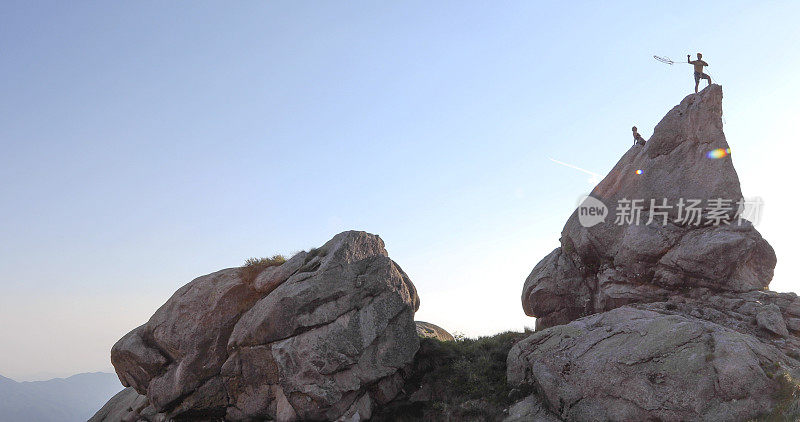 远处两名攀登者登上岩壁顶峰，日出的景象