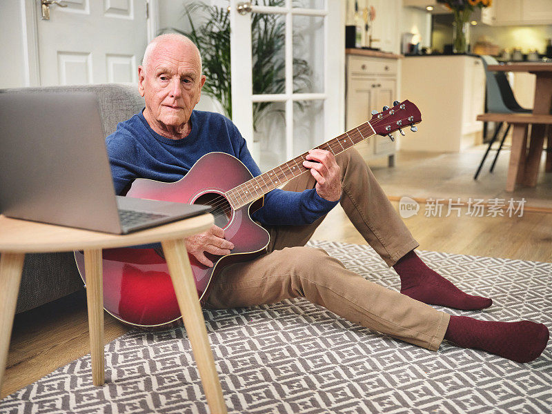 一名年长男子在家里用笔记本电脑弹奏原声吉他
