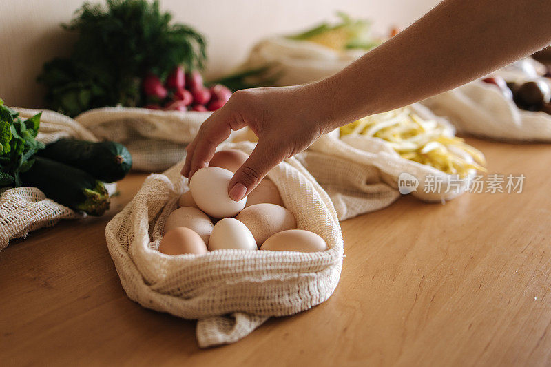 女手拿鸡蛋从帆布杂货袋。蔬菜装在可重复使用的环保棉袋里，放在木桌上。零浪费购物理念。塑料免费项目
