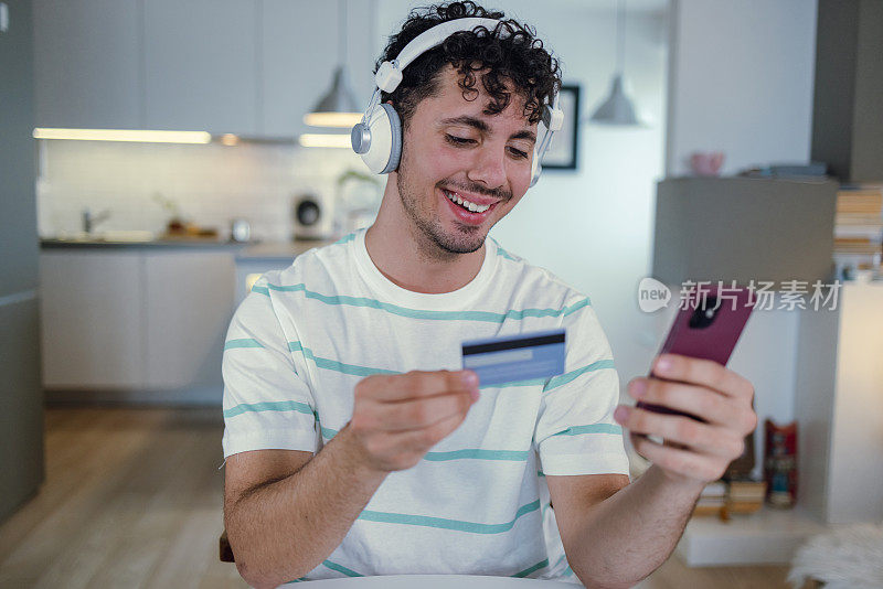 一个年轻人正在家里用信用卡通过手机进行网上购物