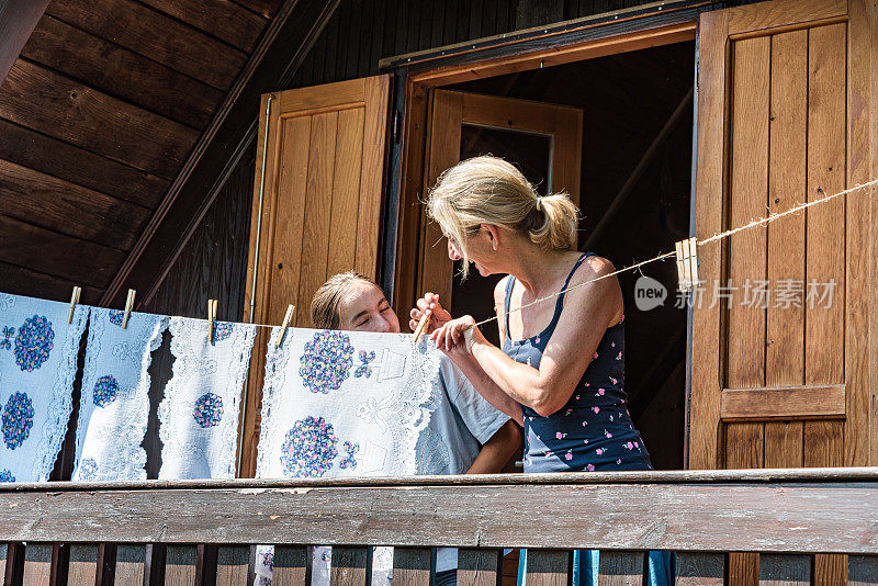 女儿在山间小屋的阳台上帮妈妈晒衣服玩得很开心