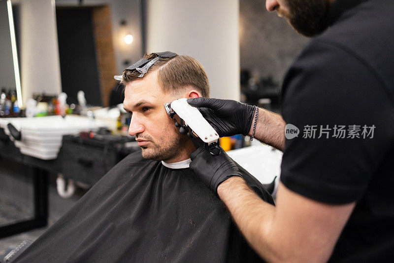 师傅在理发店为男士理发，理发师为年轻人理发