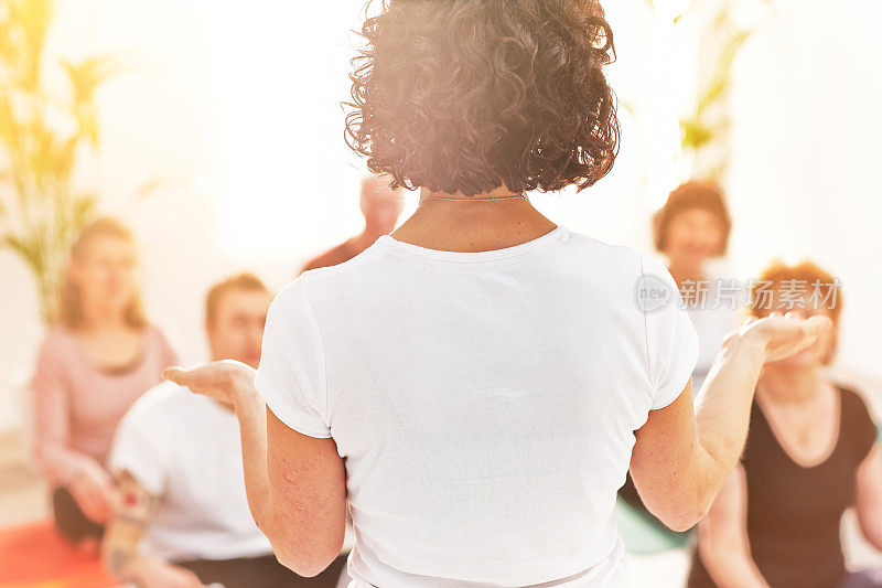 在一个健康和健康中心，瑜伽教练给一个班级上课的后视图。女教师在冥想课上给她的学生上冥想技巧的教学课