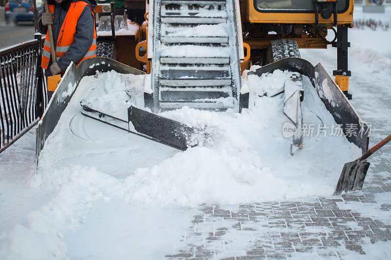 拖拉机正在清扫道路上的积雪。挖掘机清理城市街道上的大量积雪。工人们在冬天清扫道路上的积雪，清扫道路上的暴风雪