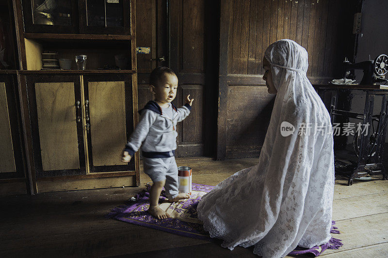 穆斯林妇女在她的孩子玩耍时祈祷