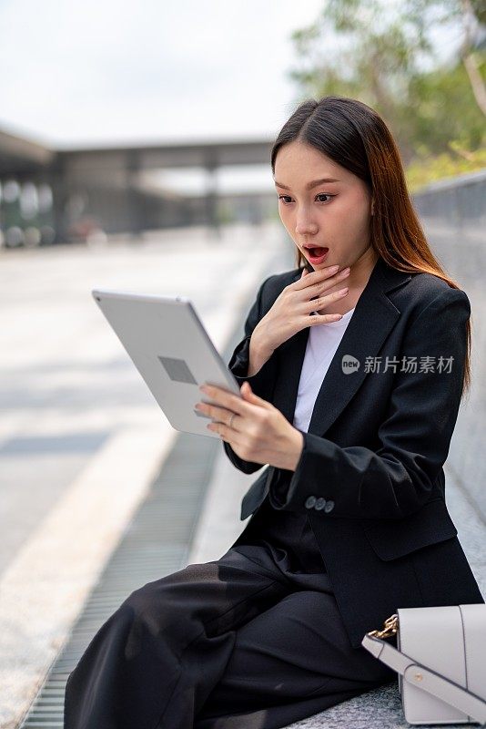 年轻美丽的亚洲女性办公室行政女员工显示难以置信的情绪后，达到收入目标，而在线上会见她的队友在她的办公大楼外的平板电脑