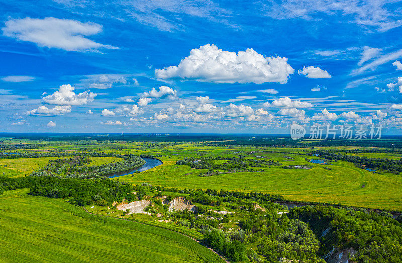 夏季景观和夏季多云天空的超摄航拍。一架无人机在河流上空飞行，周围是田野。美丽的广角镜头拍摄的夏天景色在一个乡村。