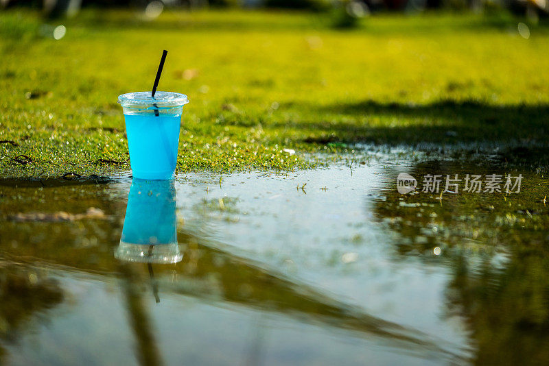 透明塑料杯是在蓝色的饮料是在草地上聚焦前景水平照片与反射