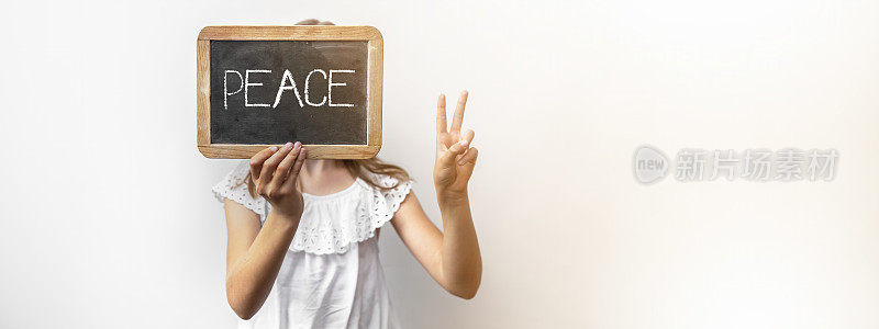小女孩拿着写有“和平”字样的学校黑板，用她的手和手指展示和平手势(胜利之手的象征)，孤立在白色背景的横幅全景上
