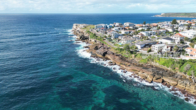 鸟瞰沿海城镇的住宅建筑和被蓝绿色海洋包围的岩石海岸