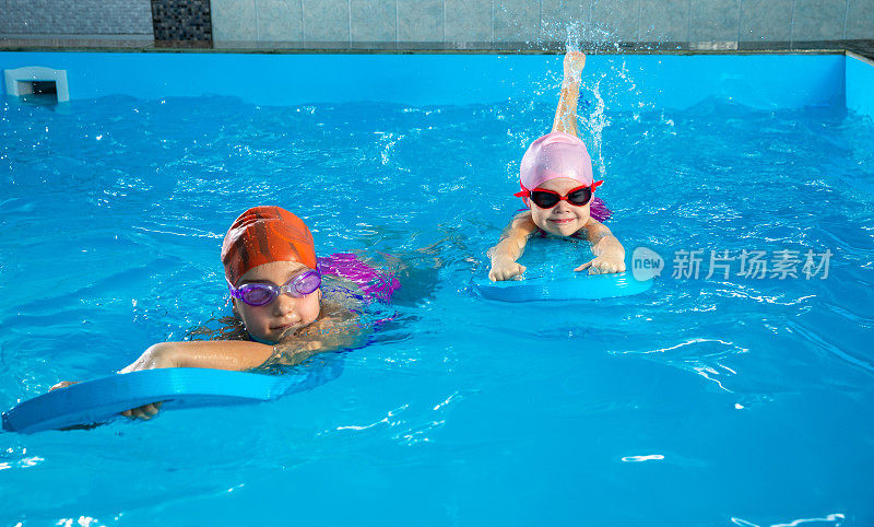 两个小女孩在泳池里玩得很开心，学习如何使用扑动板游泳
