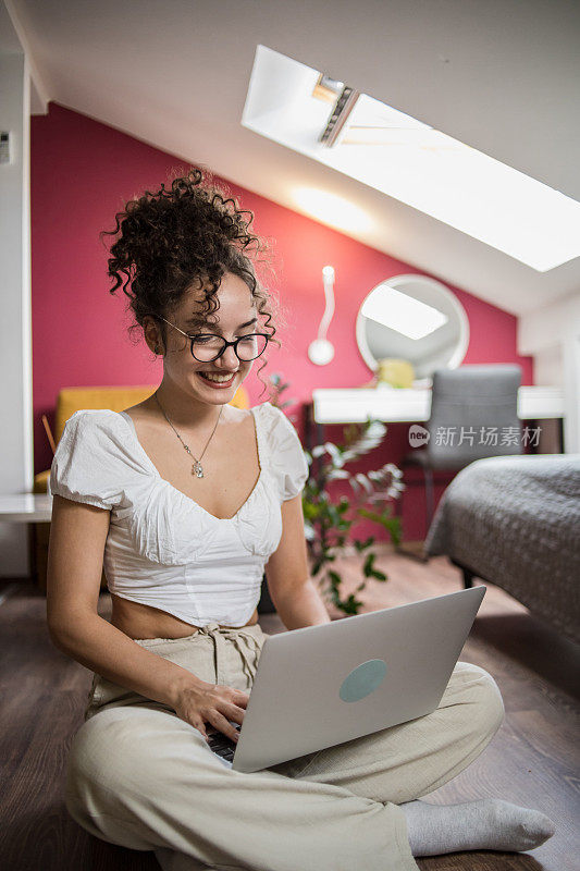 一个年轻的学生在她的公寓里学习，看着笔记本电脑和她旁边的书和论文