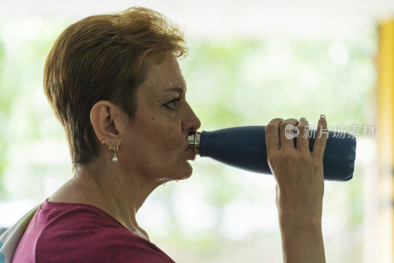 成年妇女锻炼时喝水从她的瓶子