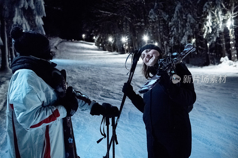 两个女人晚上在灯火通明的滑雪坡上聊天。