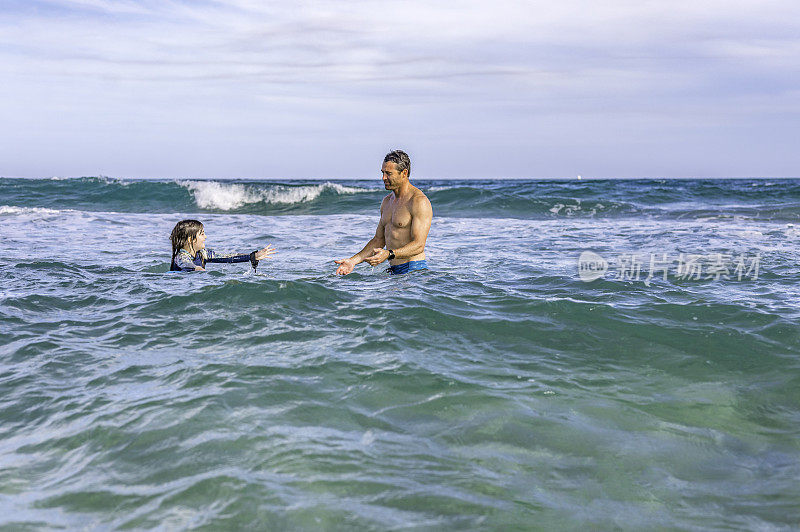 在一次热带度假中，爸爸和女儿一起玩耍，教她如何在海里冲浪