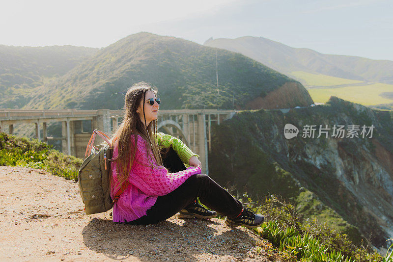 一名女子旅行者放松与风景秀丽的比克斯比溪桥在大苏尔，加利福尼亚