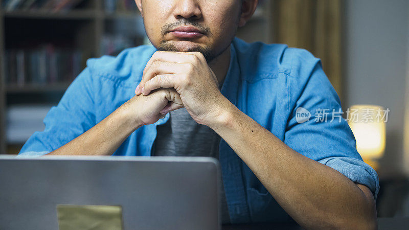 亚洲男子看着笔记本电脑，担心地皱着眉头，因为他在网上被骗了钱。