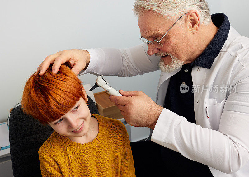 在听力诊所耳部检查呈阳性的红发男童。耳鼻喉科医生用耳镜检查男孩的耳朵