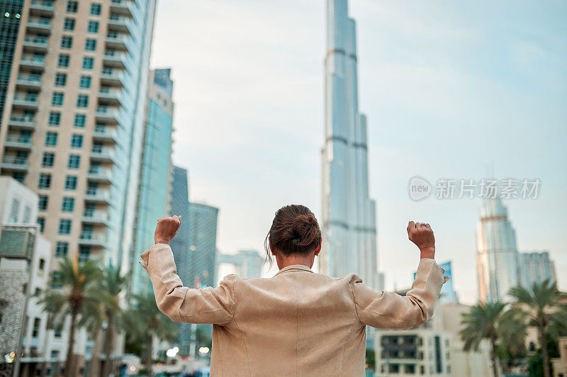 后视图，在市中心的建筑物前，欣喜的女商人举起双臂