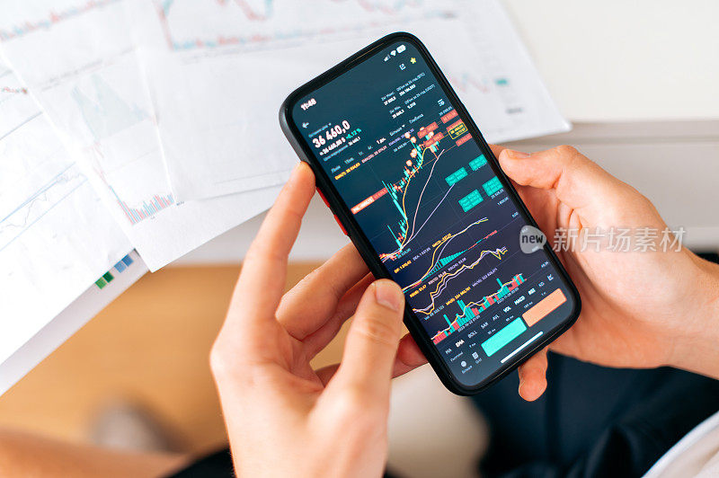 男性手中的智能手机特写，屏幕上显示交易数据指数图表，手机应用分析加密货币市场。在线交易