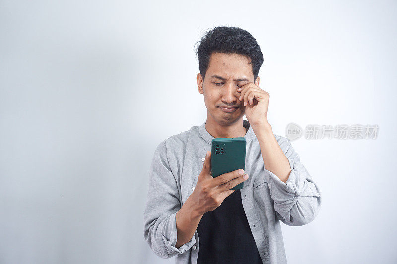 一个哭泣的男人正在看手机上的短信。网络欺凌信息