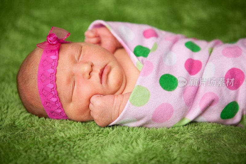 新生女婴戴着头巾，睡在圆点毯子里