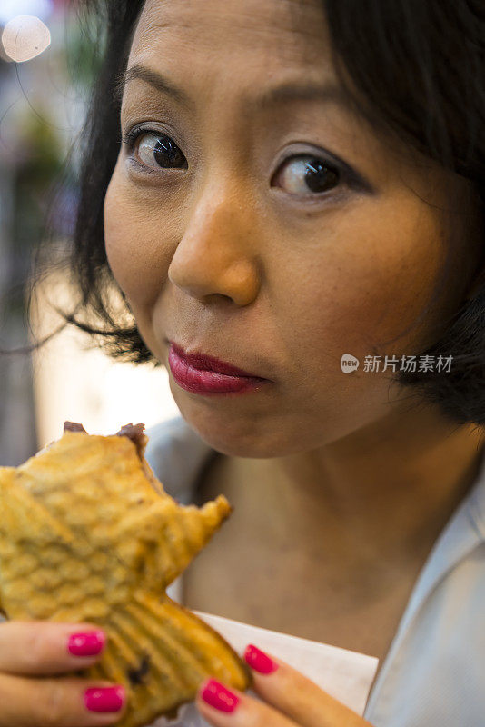 日本京都，一名妇女在街上吃Taiyaki。