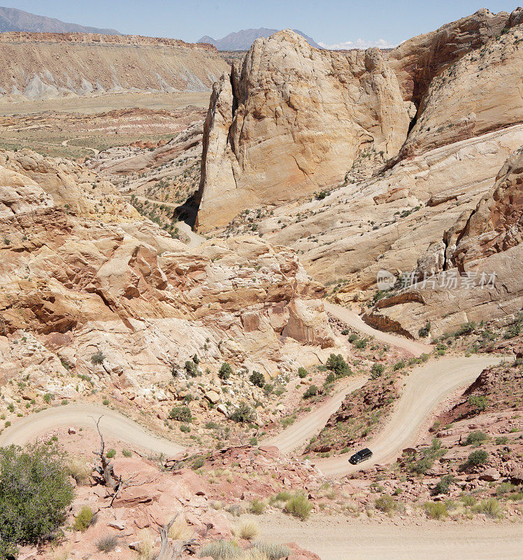 越野车行驶在一条穿越悬崖的曲曲折折的土质沙漠道路上