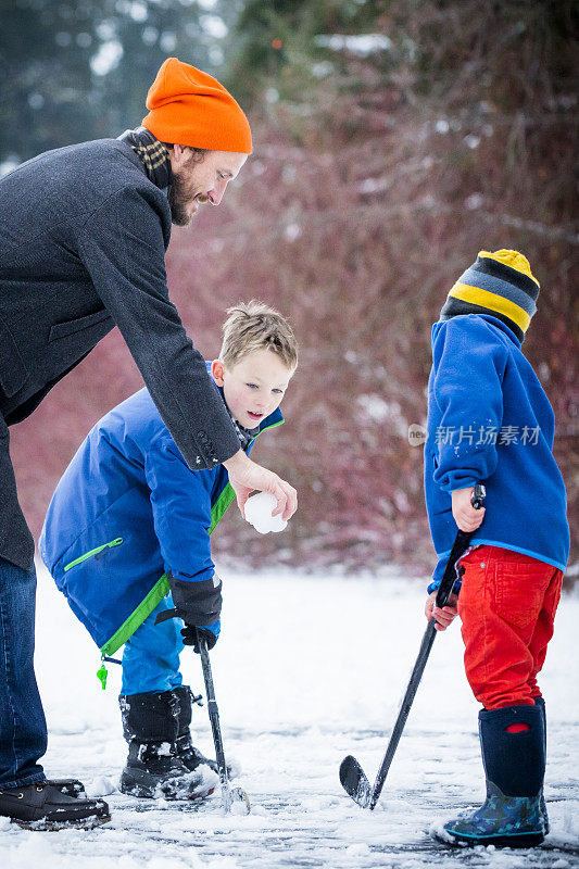 年轻的家庭在外面的雪地里打池塘曲棍球。