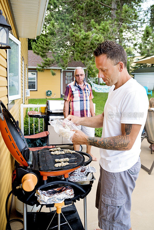 父亲和成年的儿子在夏季家庭烧烤烹饪。