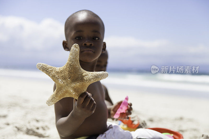 一个非洲男孩在海滩上抱着一条海星
