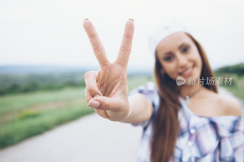 微笑的年轻女子在乡村道路上做和平标志