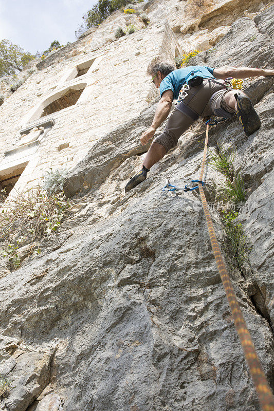 攀岩者攀登垂直悬崖下的石头住所