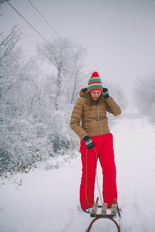 女孩在森林里散步，拉雪橇。一个开心的女人。圣诞假期。女孩免费休息。圣诞树躺在雪橇上。美丽的年轻女孩或女人在森林里散步。拉木制雪橇