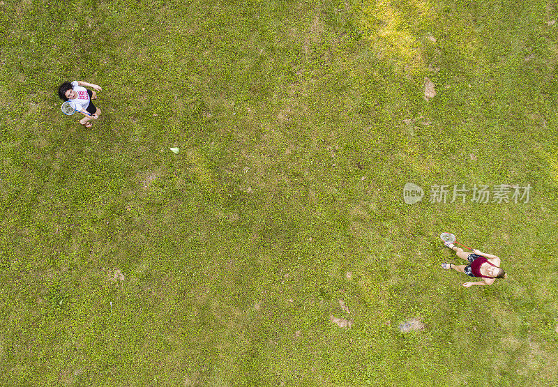 两个女人在草坪上打羽毛球。俯视图正上方，无人机拍摄