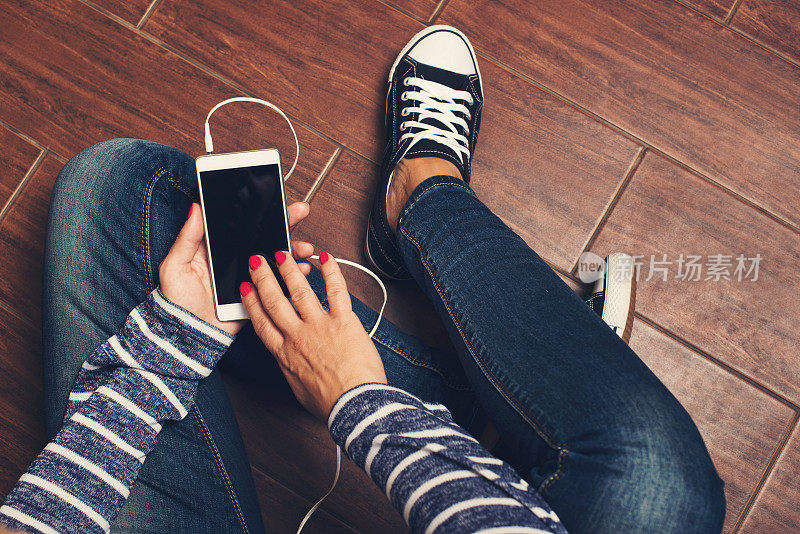 穿着运动鞋的女孩坐在地板上，手里拿着智能手机。